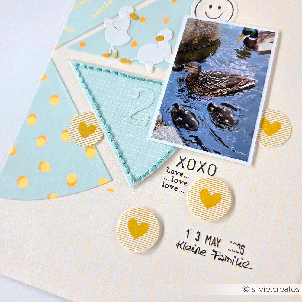 Eine Scrapbook-Seite mit einem Foto einer Entenfamilie, Herzaufklebern, Pastellfarben und dem Schriftzug „Kleine Familie“ – alles wunderschön auf bezauberndem Designpapier arrangiert, das der Seite eine ganz besondere Note verleiht.