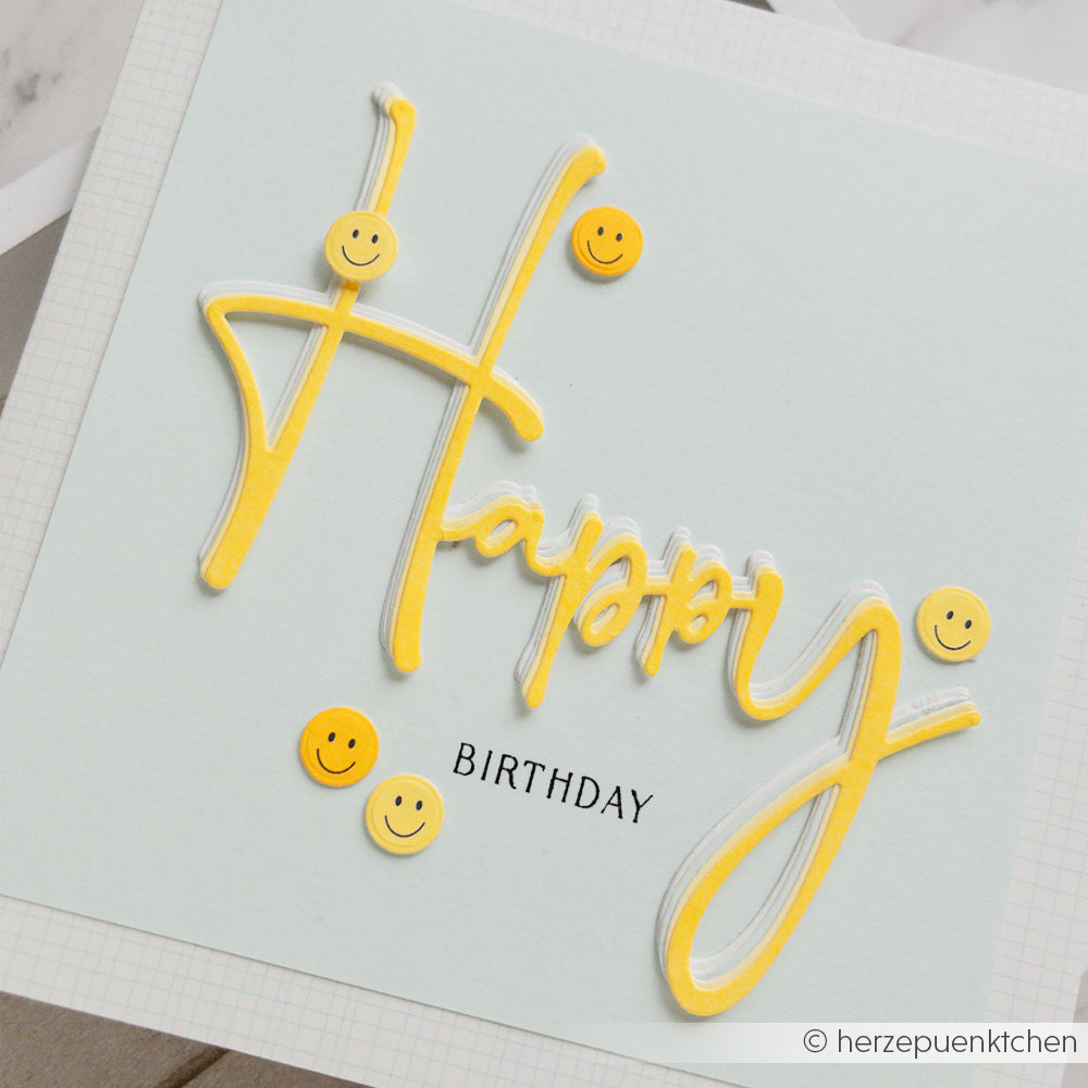 Geburtstagskarte mit der Aufschrift „Happy“ in gelber Schreibschrift und Smiley-Aufklebern sowie dem Schriftzug „Birthday“ in Schwarz. Diese fröhliche Karte eignet sich perfekt für Papierprojekte und kommt auf Neonpapier besonders gut zur Geltung – für einen besonders festlichen Touch.