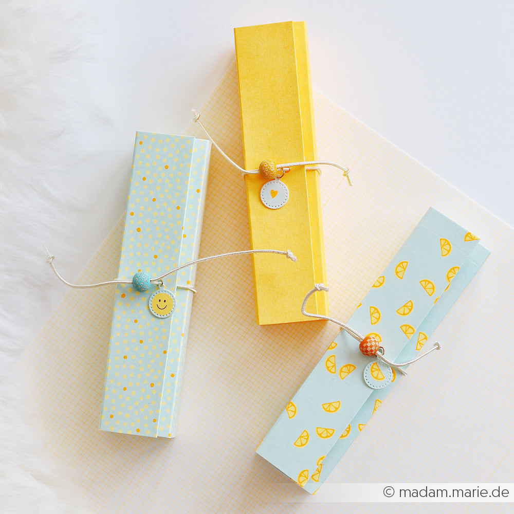 Drei rechteckige, pastellfarbene Geschenkboxen mit Mustern, die mit weißer Schnur und Zierperlen verziert sind und aus stilvollem Designpapier gefertigt wurden – für den perfekten Mimi-Sommer-Special-Touch.
