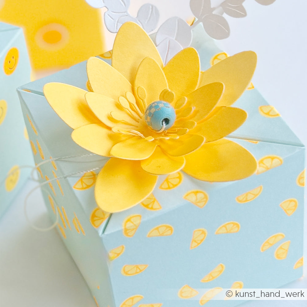 Hellblaue Geschenkbox mit gelben Zitronenscheiben-Mustern, verziert mit einer gelben Papierblume und einer blauen Perle in der Mitte – perfekt für Ihre „Neon Papier“- oder „Designpapier“-Papierprojekte.