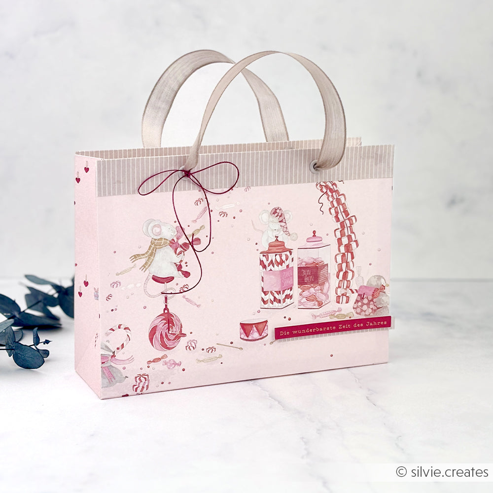 Rosa Geschenktüte mit Mäusen und Süßigkeiten, verziert mit dem deutschen Ausdruck für die schönste Zeit.