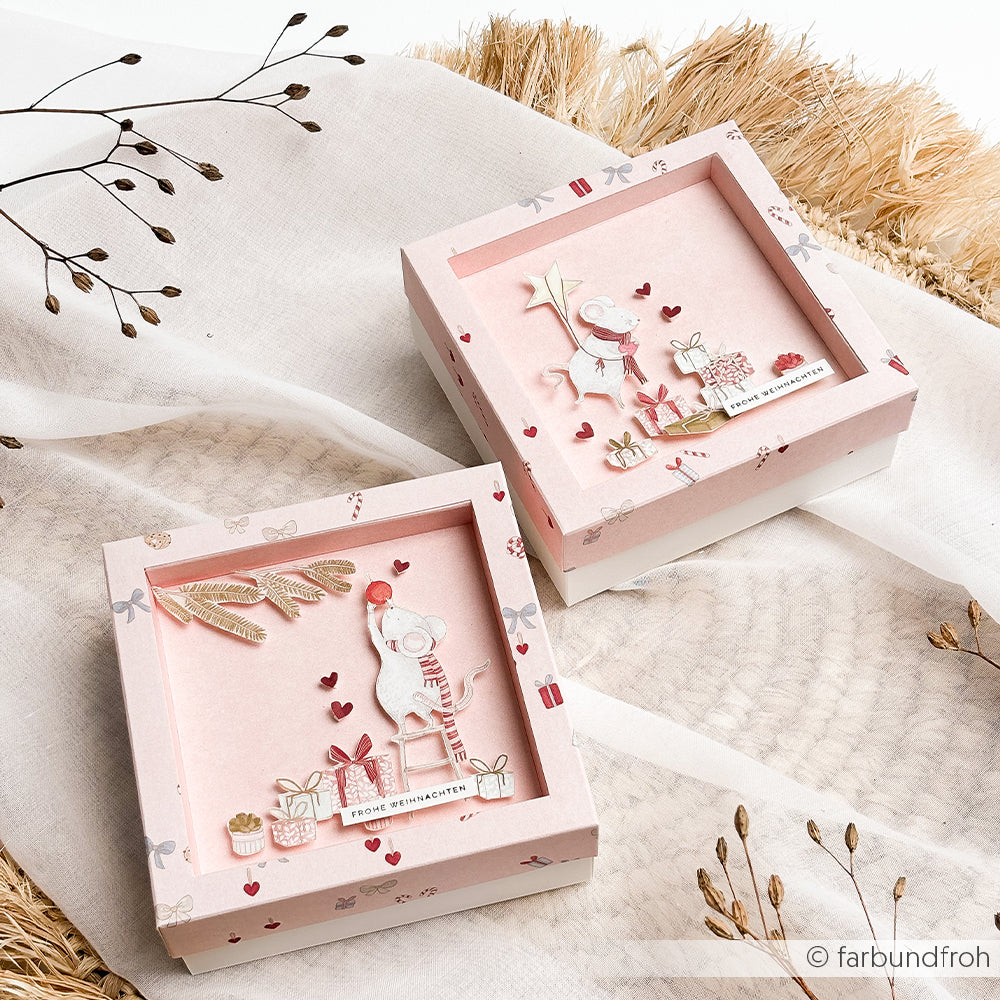 Zwei quadratische, rosa Schachteln mit mehrschichtigen Motiven aus Designpapier, die Mäuse mit Weihnachtsgeschenken zeigen.