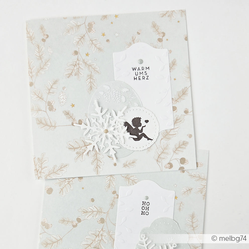 Zwei handgefertigte Grußkarten mit ausgeschnittenen Schneeflocken, einer Cherub-Silhouette und Text aus Designpapier.