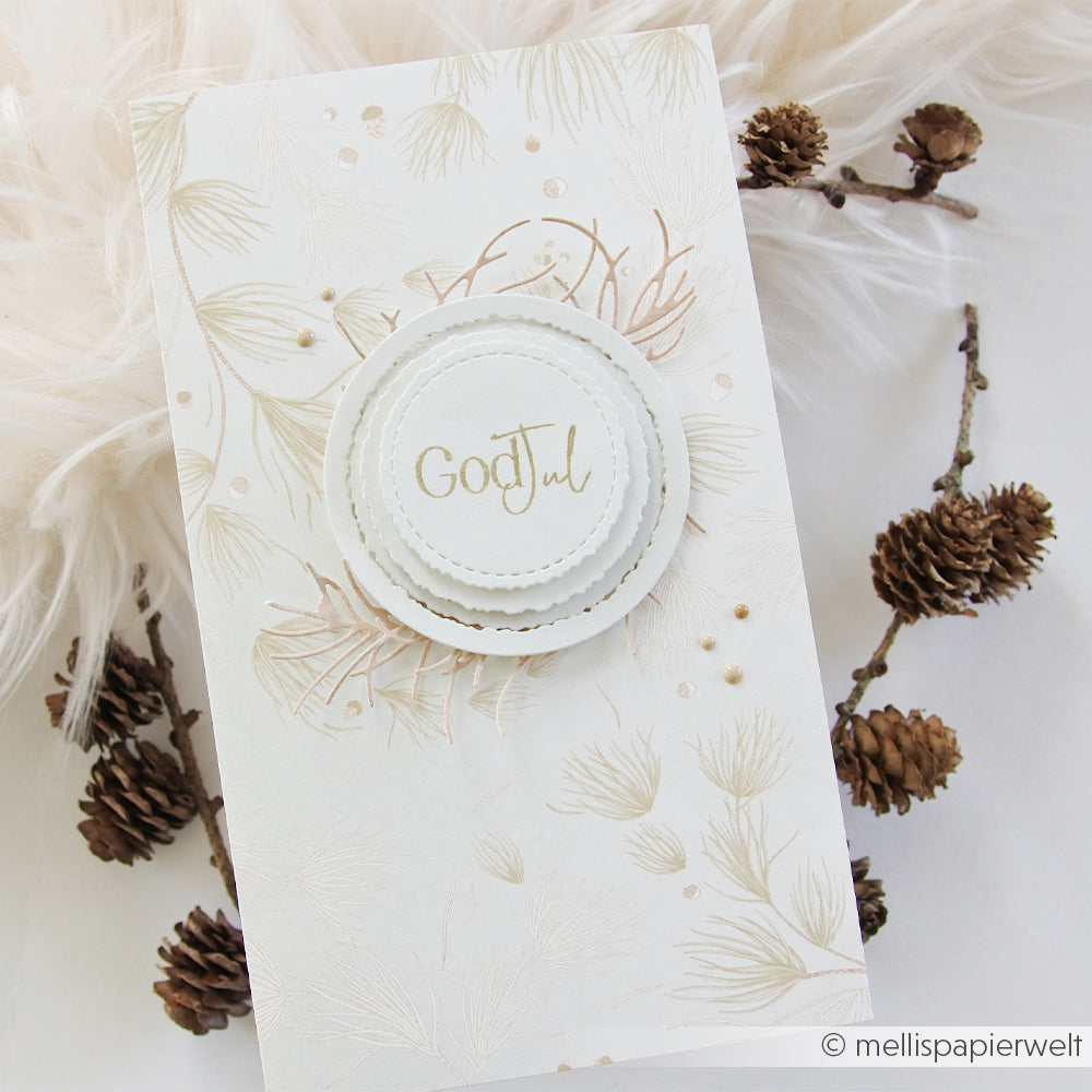 Handgefertigte Weihnachtskarte aus Designpapier mit goldenem God Jul-Schriftzug, Tannennadeln und Tannenzapfen.