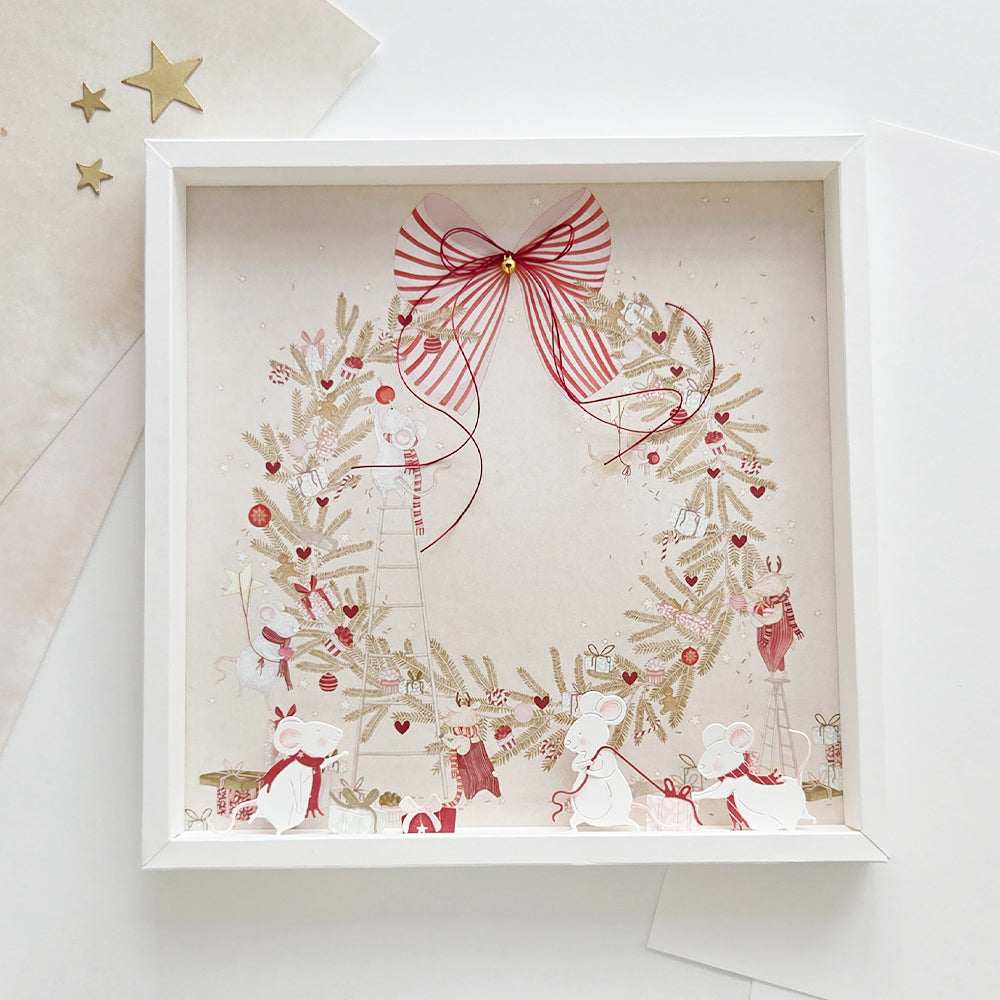 Gerahmte Illustration von Mäusen, die einen Weihnachtskranz mit einer rot gestreiften Schleife schmücken – als Vorlage für Bastelarbeiten aus Papier.