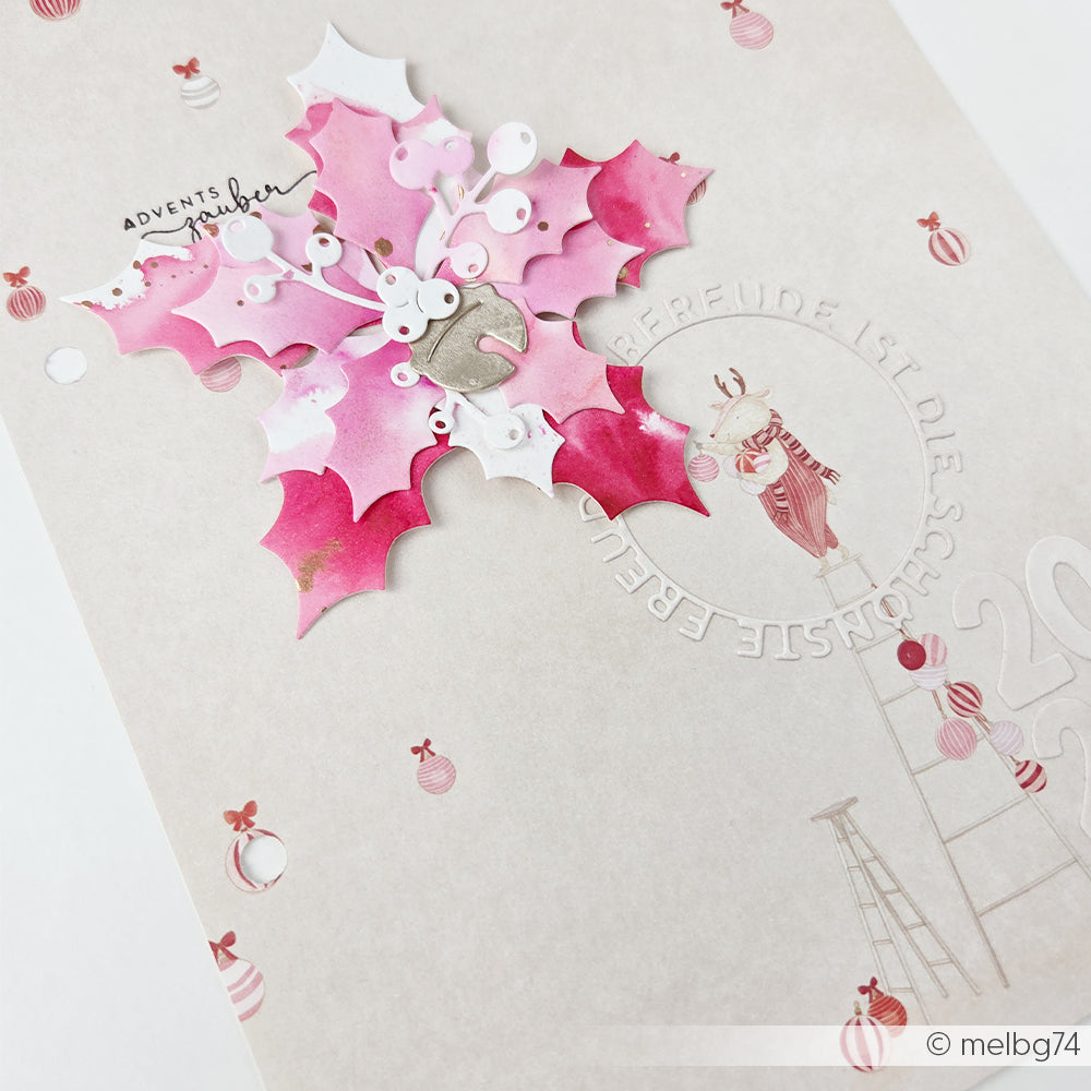 Eine rosa, ausgestanzte Weihnachtssternblüte auf einer Weihnachtskarte mit einem Rentier auf einer Leiter, gestaltet mit Bastelpapier.
