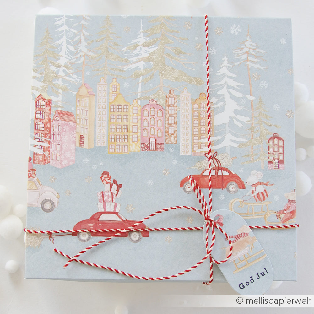 Geschenkbox, verpackt in Designpapier mit Weihnachtsmäuse-Motiv, einer winterlichen Dorfszene und einem God Jul-Anhänger.