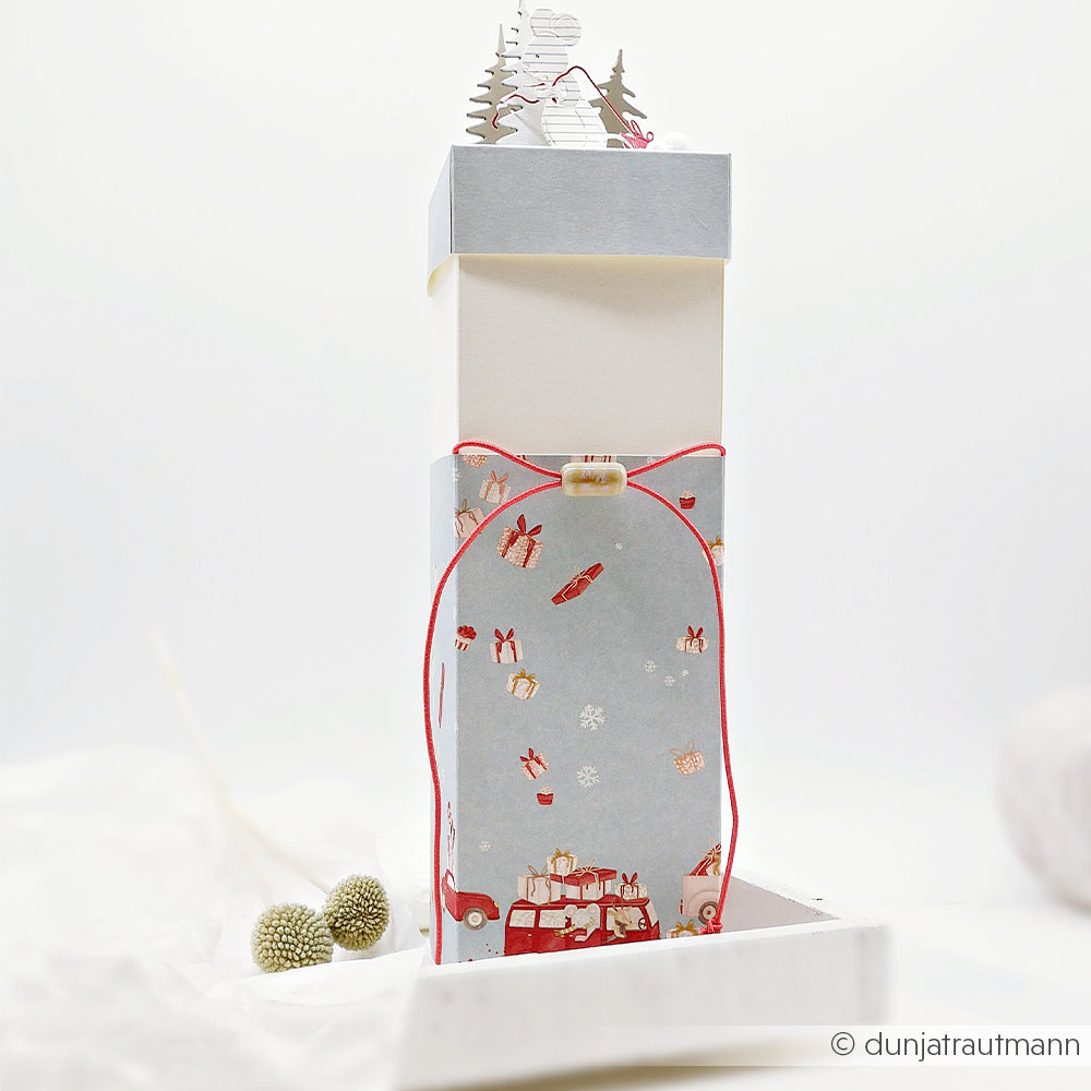 Hohe Geschenkbox aus Papier im Weihnachtsmaus-Design mit weihnachtlichen Motiven und einem Hirsch als Aufsatz.