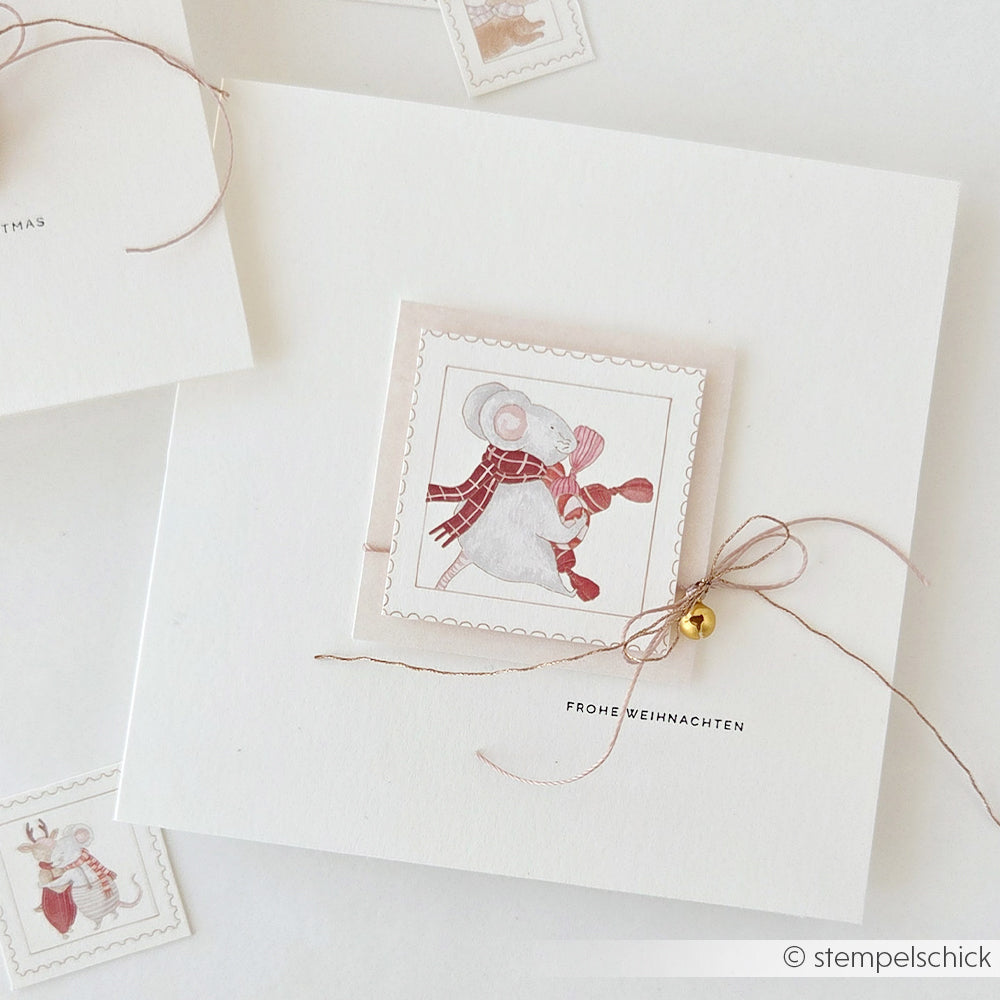 Eine Grußkarte mit einer Aquarellillustration einer „Weihnachtsmäuse“-Maus, die einen Schal trägt, der mit einer Schnur zusammengebunden ist und an dem ein kleines goldenes Glöckchen hängt.