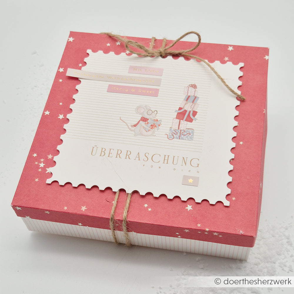 Rote Geschenkbox mit einer Grußkarte, auf der Mäuse, Geschenke und das Wort ÜBERRASCHUNG abgebildet sind.
