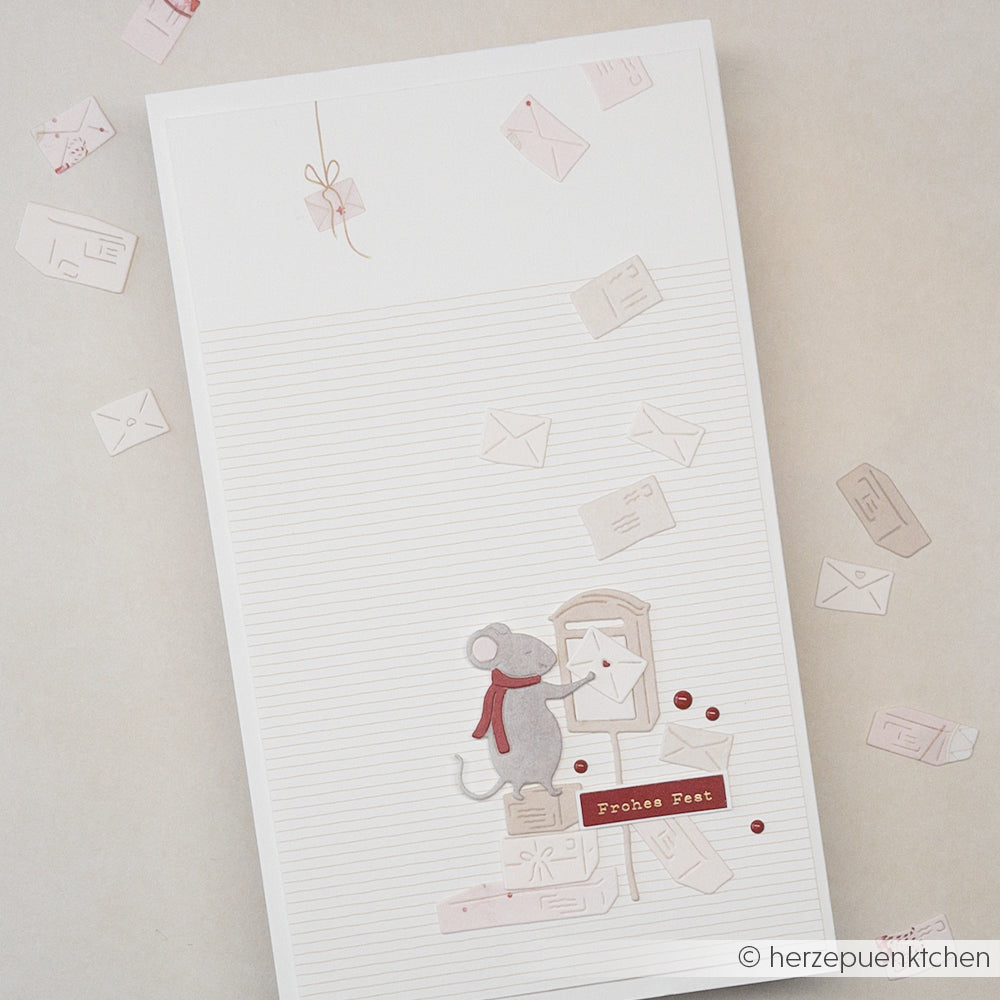 Eine Maus mit rotem Schal wirft einen Brief in einen Briefkasten auf Papier mit einem weihnachtlichen Mausmotiv.