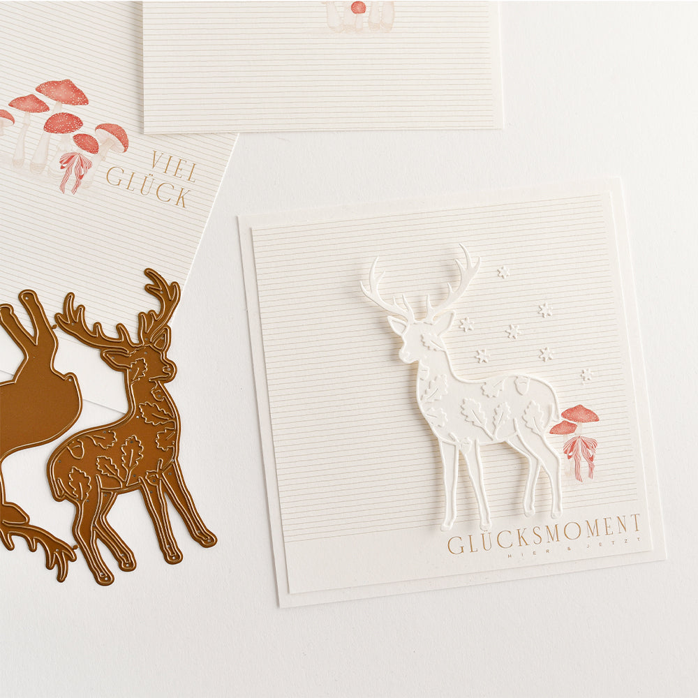 Grußkarten aus Designpapier mit ausgestanzten Hirsch- und Pilzmotiven, ergänzt durch die deutschen Schriftzüge „Viel Glück“ und „Glücksmoment“.