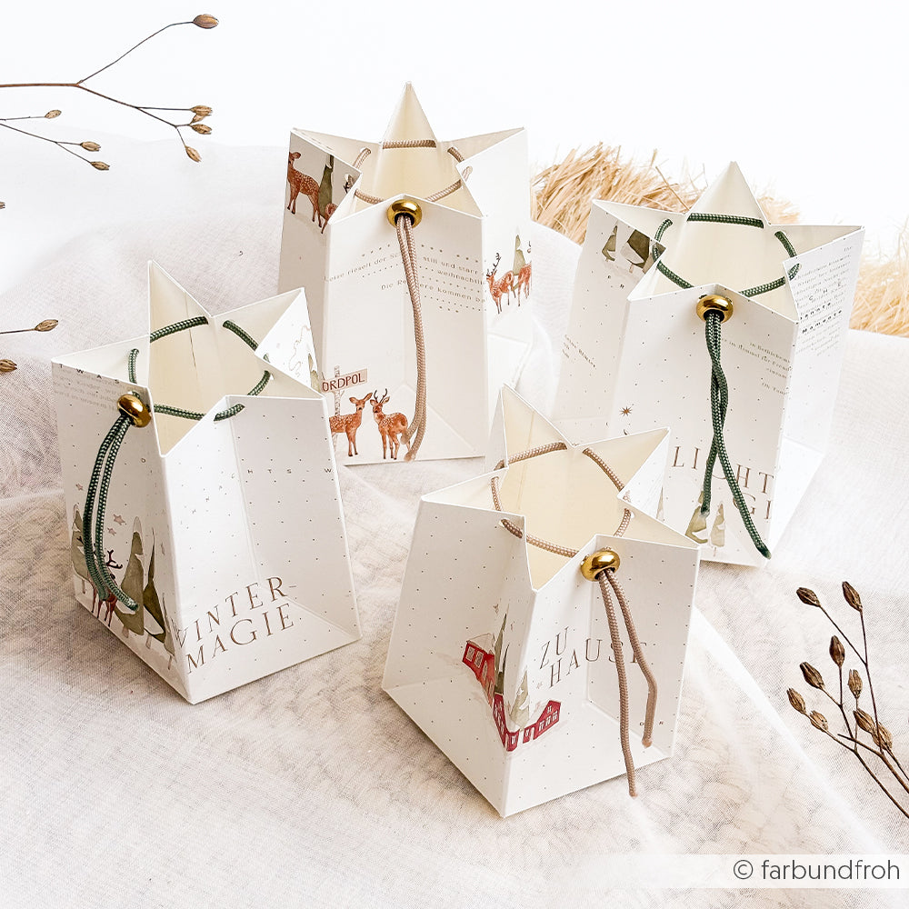Vier sternförmige Geschenktüten aus weißem Papier mit Motiven vom Nordpol und Kordelgriffen.