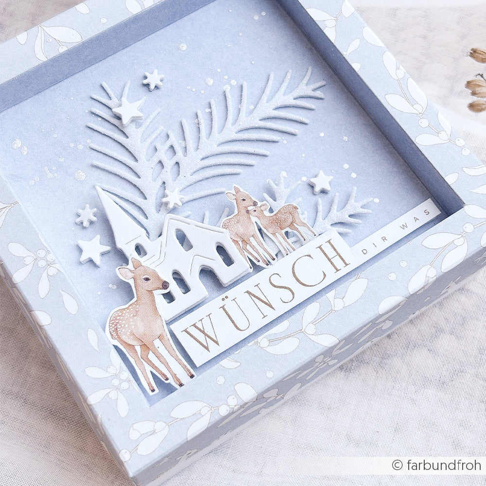 Eine Schattenbox mit Papierhirschen, einem Haus und Sternen, verziert mit Designpapier und dem Schriftzug WÜNSCH DIR WAS.