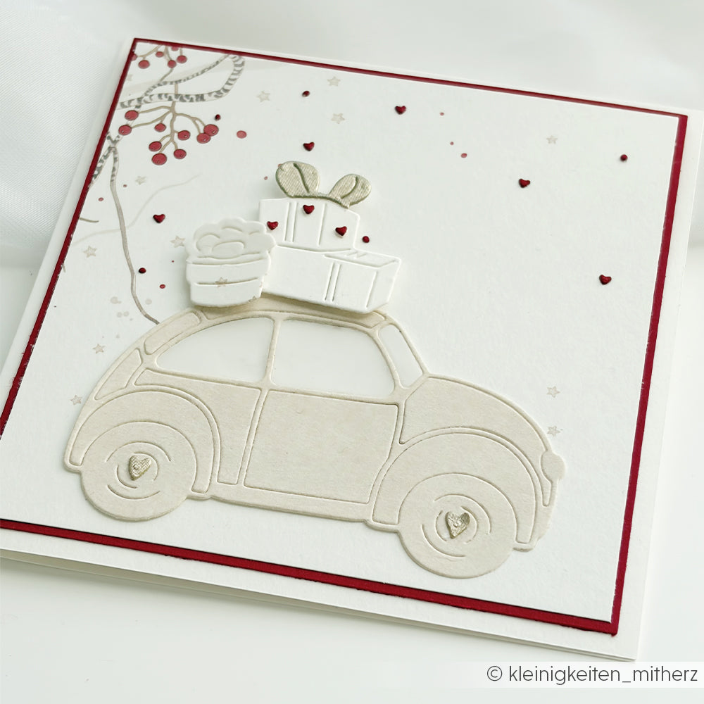 Handgefertigte Karte mit einem Oldtimer, auf dessen Dach Geschenke liegen, und Herzmotiven auf Designpapier.