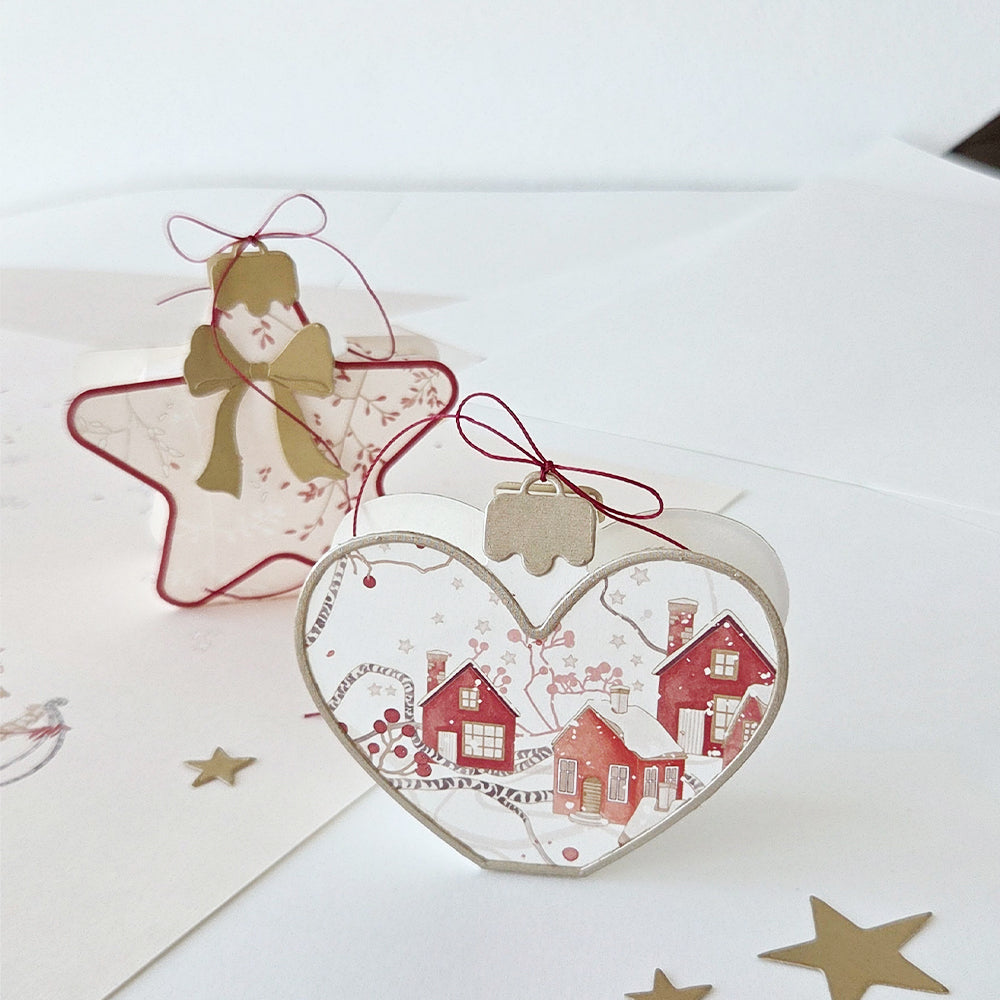 Herz- und sternförmige Weihnachtsanhänger aus Papier mit rotem Winterdorf-Motiv.