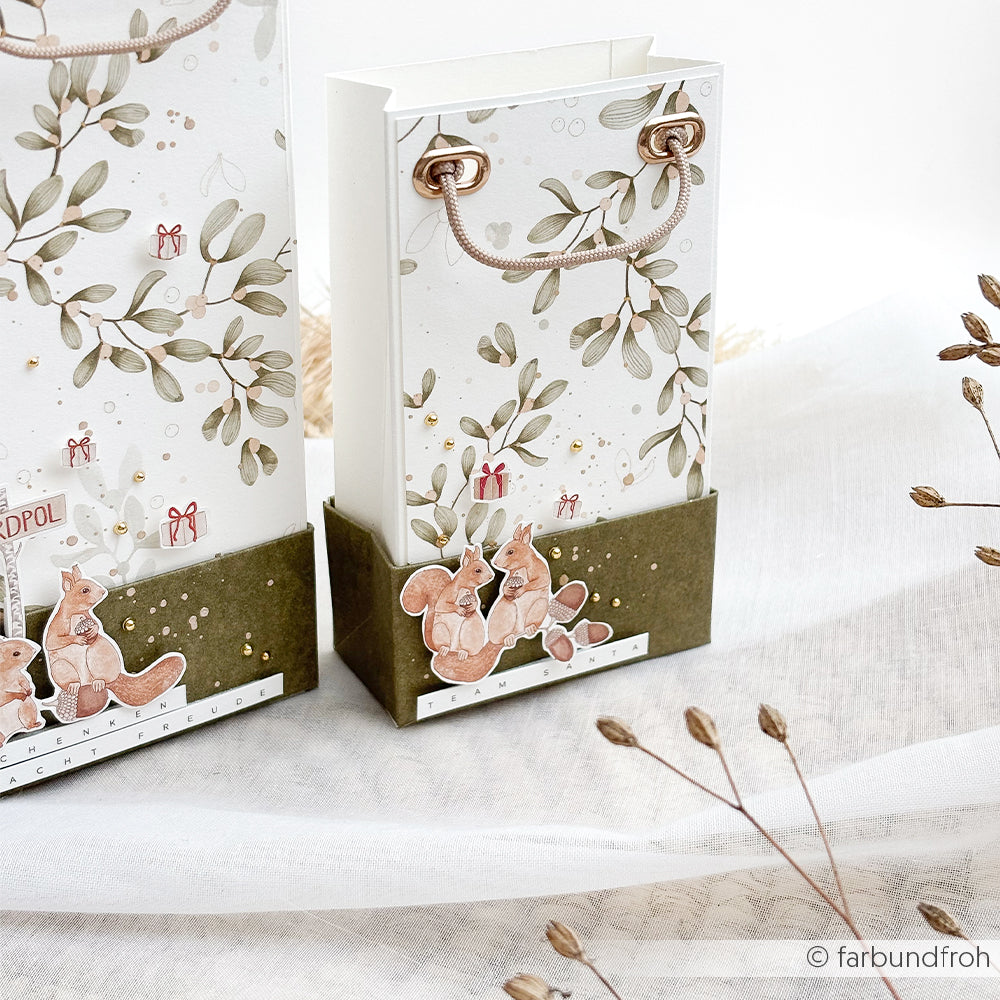 Zwei Geschenktüten mit Illustrationen von Eichhörnchen und Mistelzweigen auf Designpapier.