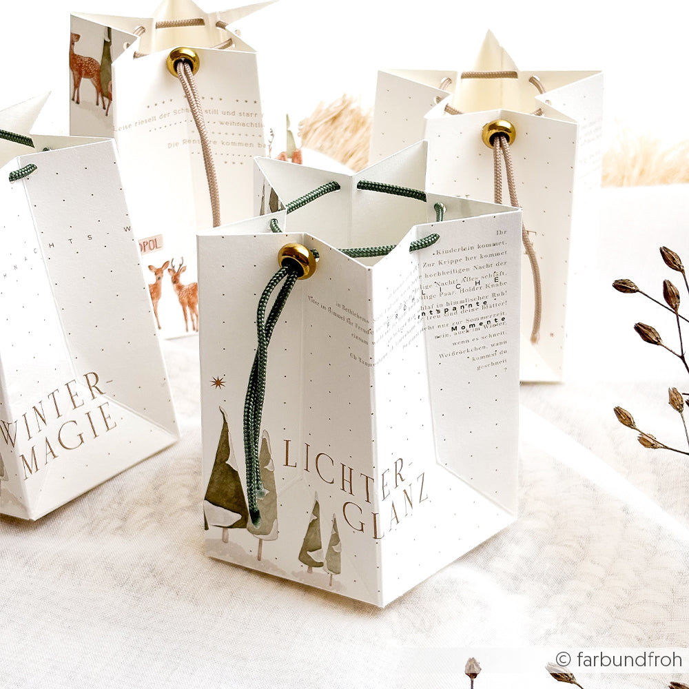 Vier weiße Tannenwald Szenen-Geschenktüten mit Hirschmotiv, deutschem Text und Kordelgriffen.
