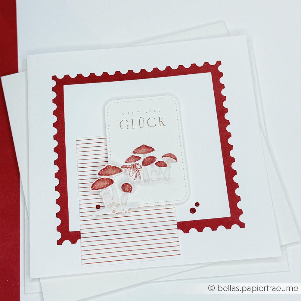 Grußkarte mit roten Pilzen, einer Schleife und dem deutschen Text Ganz viel Glück für Papierprojekte.