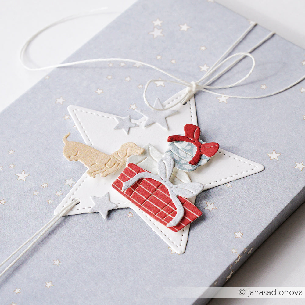 Eine Geschenkbox aus Kleine Sterne auf Denim Hell-Papier mit einem sternförmigen Geschenkanhänger, auf dem ein Hund abgebildet ist.