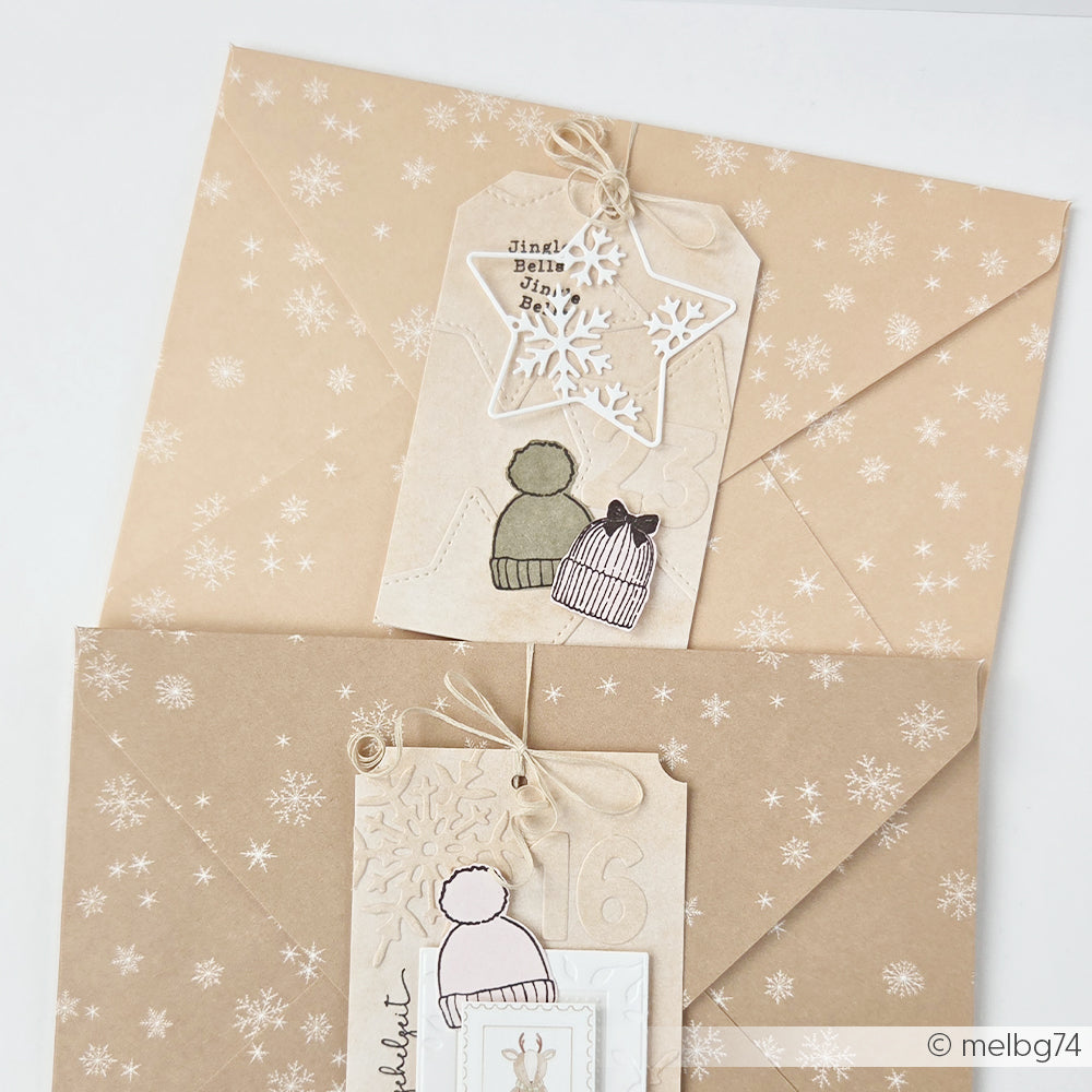 Zwei Geschenkanhänger mit Abbildungen von Wintermützen und Schneeflockenmotiven auf gemustertem Designpapier.