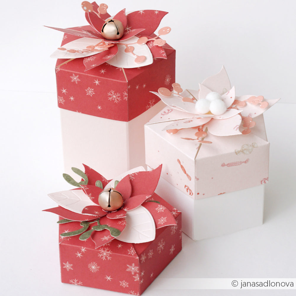Drei hochwertige rote Geschenkboxen, verziert mit Papier-Weihnachtssternen, Glöckchen und Schneeflocken.