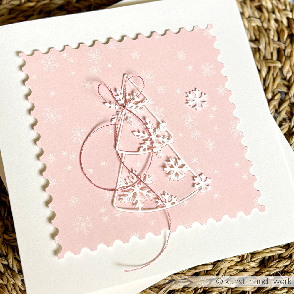 Handgefertigte Grußkarte mit einem quadratischen Motiv mit rosa Schneeflockenmuster, weißen, ausgestanzten Weihnachtsbäumen und einer rosa Schnur für diese „Papierprojekte“.
