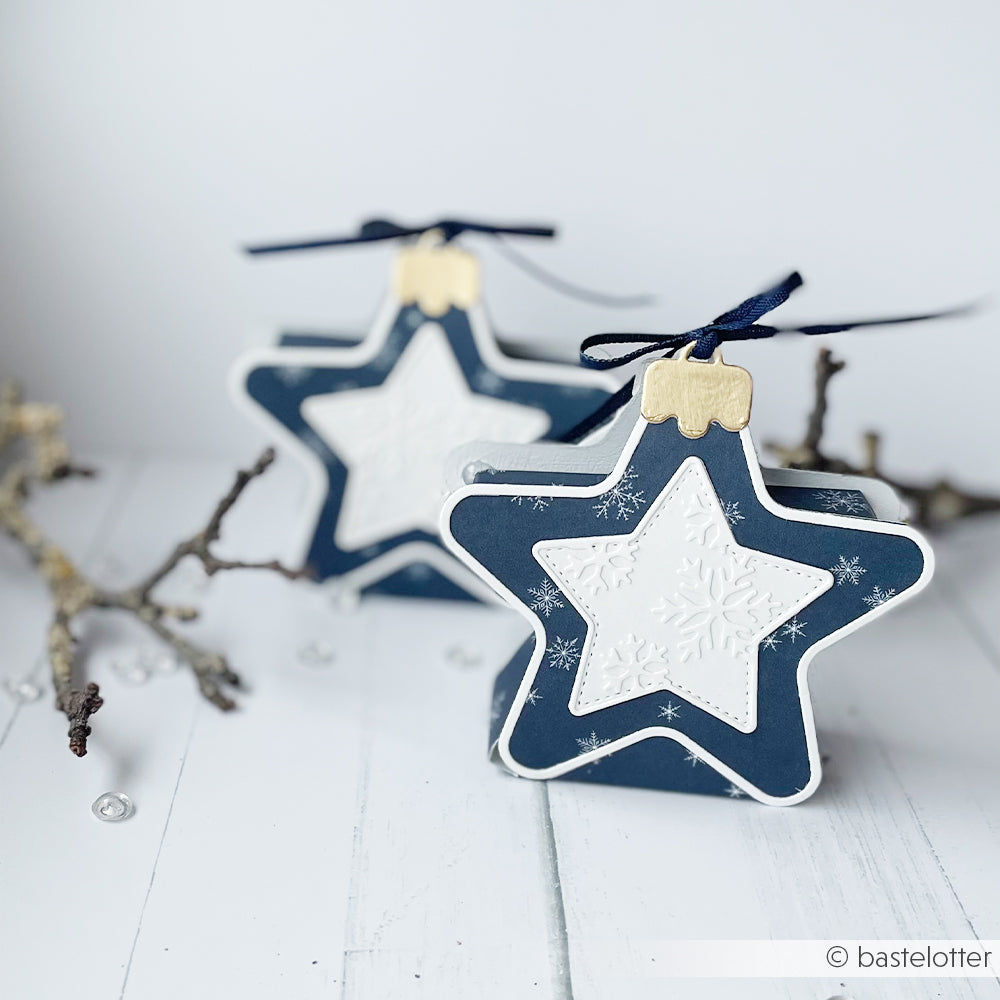 Zwei marineblaue und weiße Premiumblau-Geschenkboxen in Sternform, verziert mit Schneeflockenmustern.