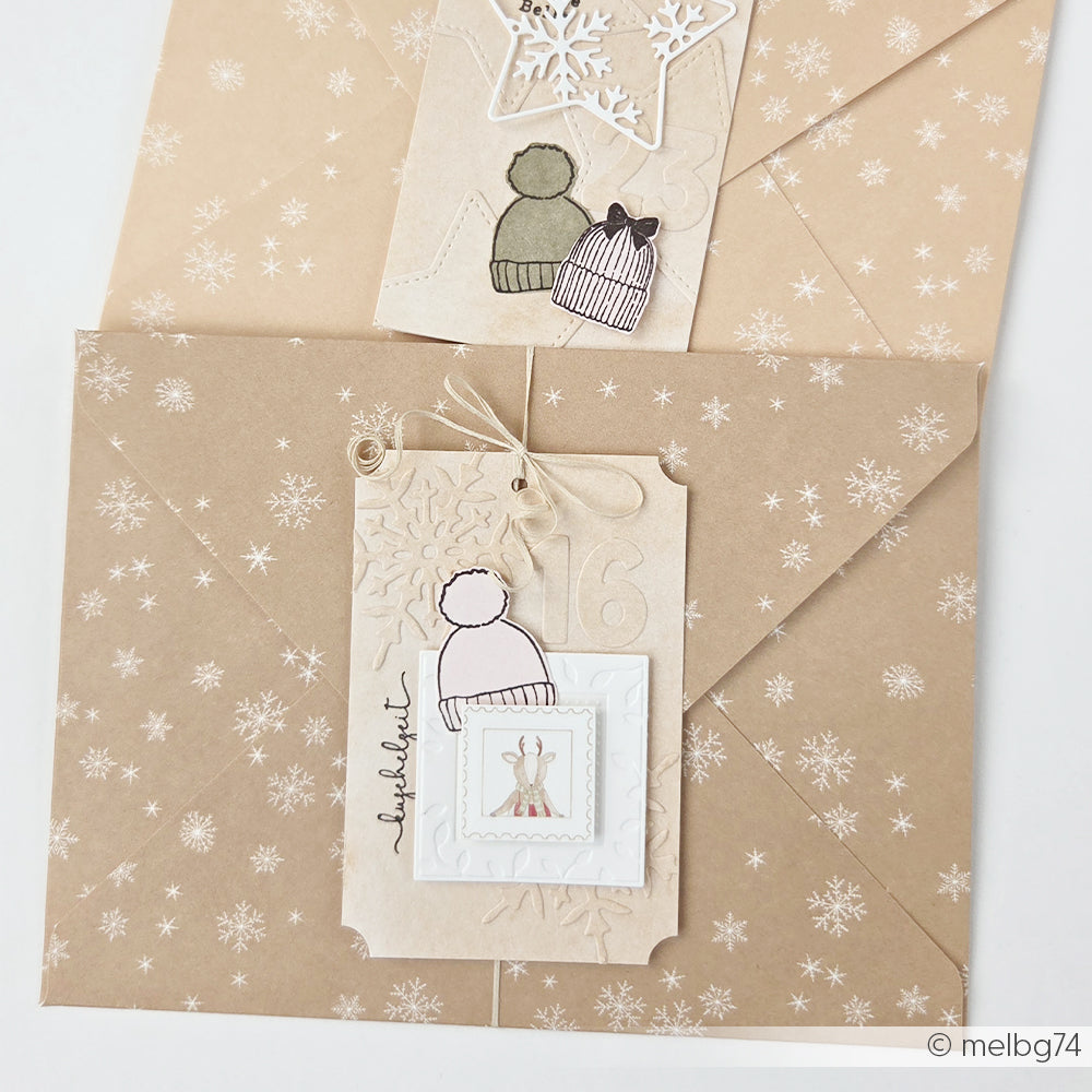 Zwei braune Umschläge mit Schneeflocken-Motiv und verzierten Geschenkanhängern aus Papier.