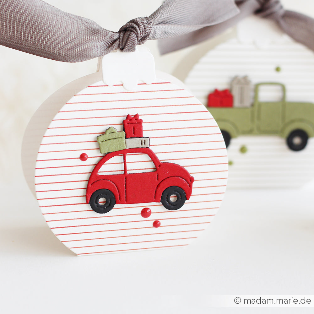 Zwei runde Ornamente mit zarten, leuchtend roten Streifen sowie Papierausschnitte eines Autos und eines Lastwagens.