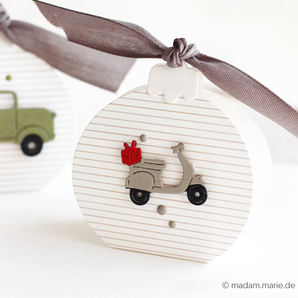 Runde, weiße Geschenkbox aus Designpapier mit einem grauen Roller und roter Geschenkbox-Verzierung.