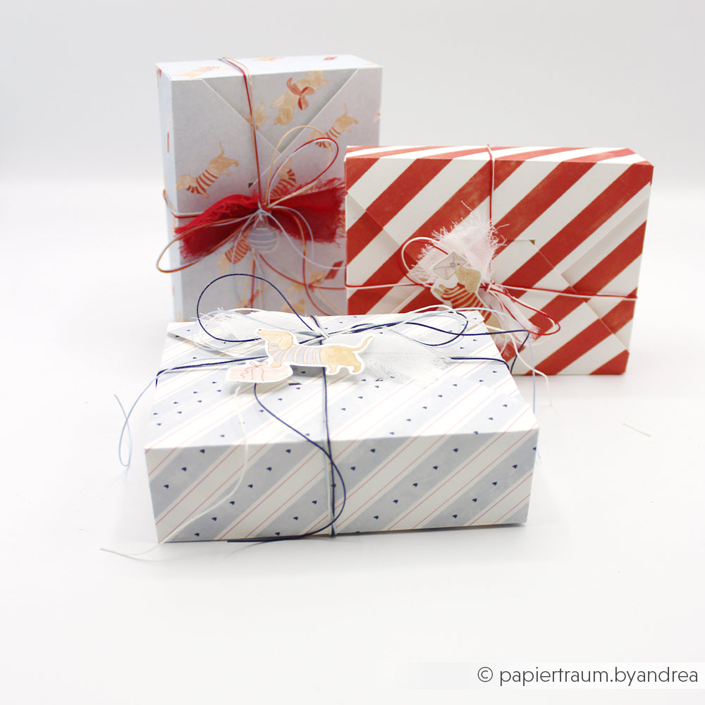 Drei Geschenkboxen, verpackt in rotem, mit Wasserfarbenstreifen bedrucktem Papier, mit Schnur und Anhängern in Form von Hunden.