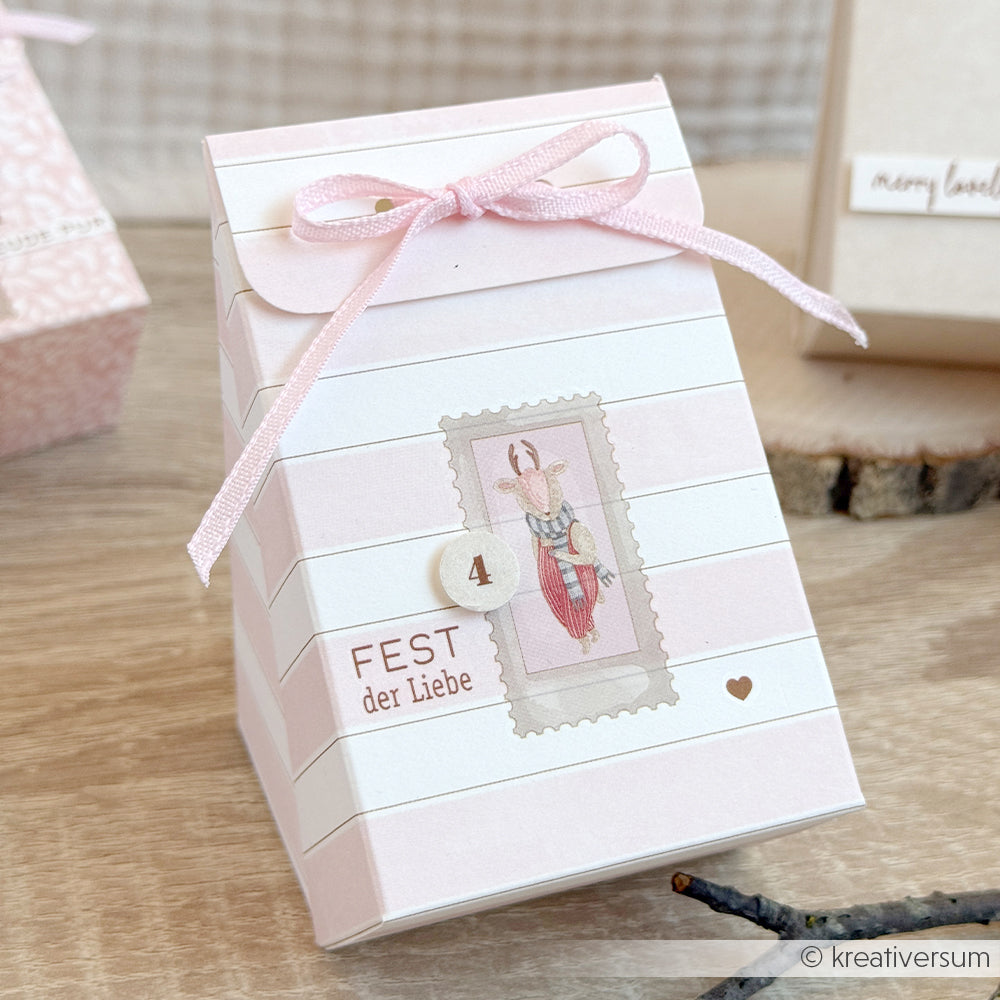 Kleine, rosa-weiß gestreifte Geschenkbox mit goldenen Akzenten, einer Schleife und einem nummerierten Hirschmotiv.