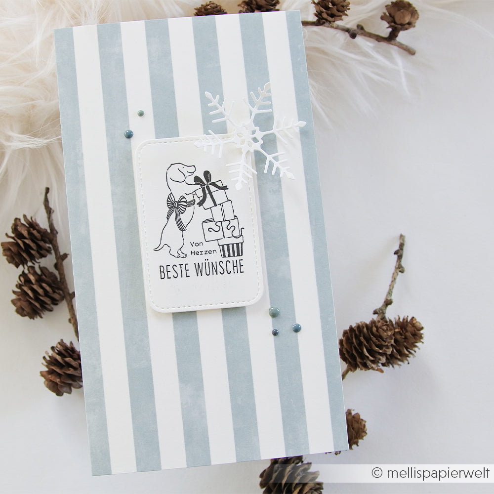 Handgefertigte Karte mit blauen Aquarellstreifen, einem Dackel mit Geschenken und einem ausgeschnittenen Schneeflöckchen.