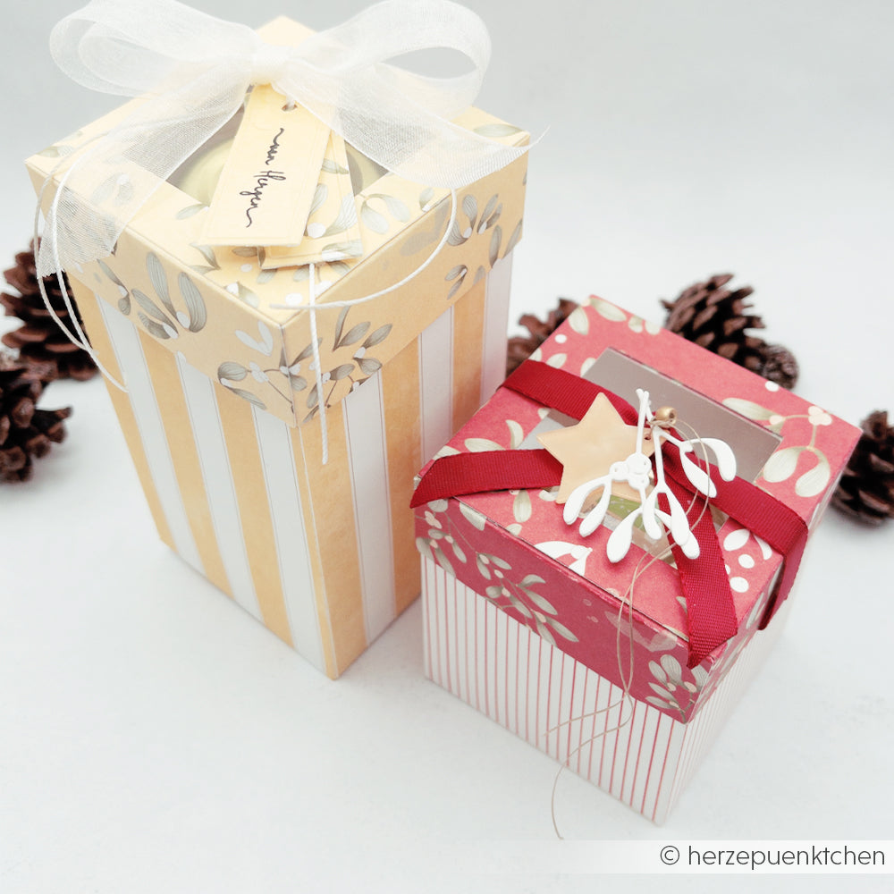 Zwei Geschenkboxen, eingepackt in gestreiftes Papier mit Aquarellmuster, verziert mit Bändern und Tannenzapfen.