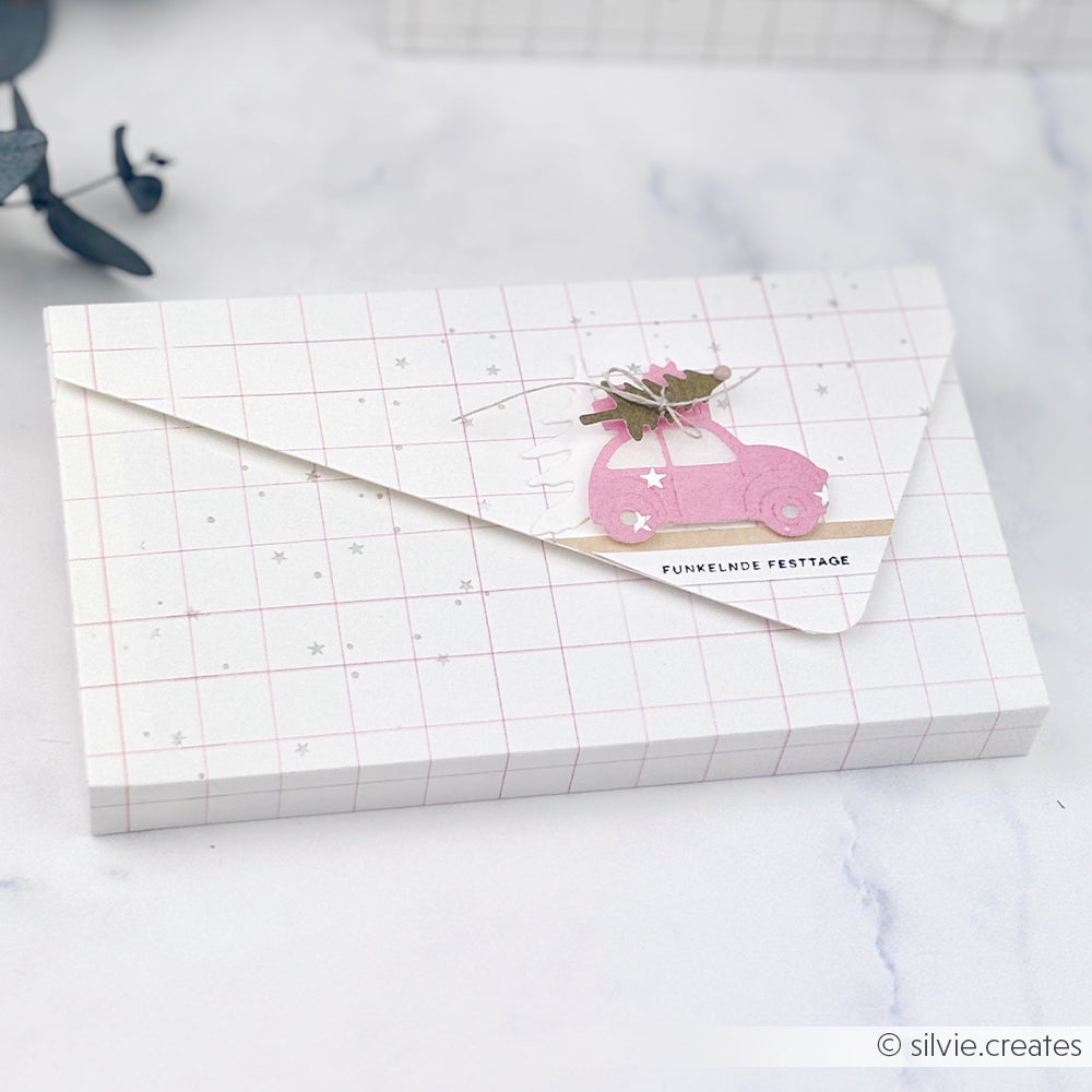 Umschlag aus Designpapier mit Karomuster, einem rosa Auto und dem Schriftzug FUNKELNDE FESTTAGE.