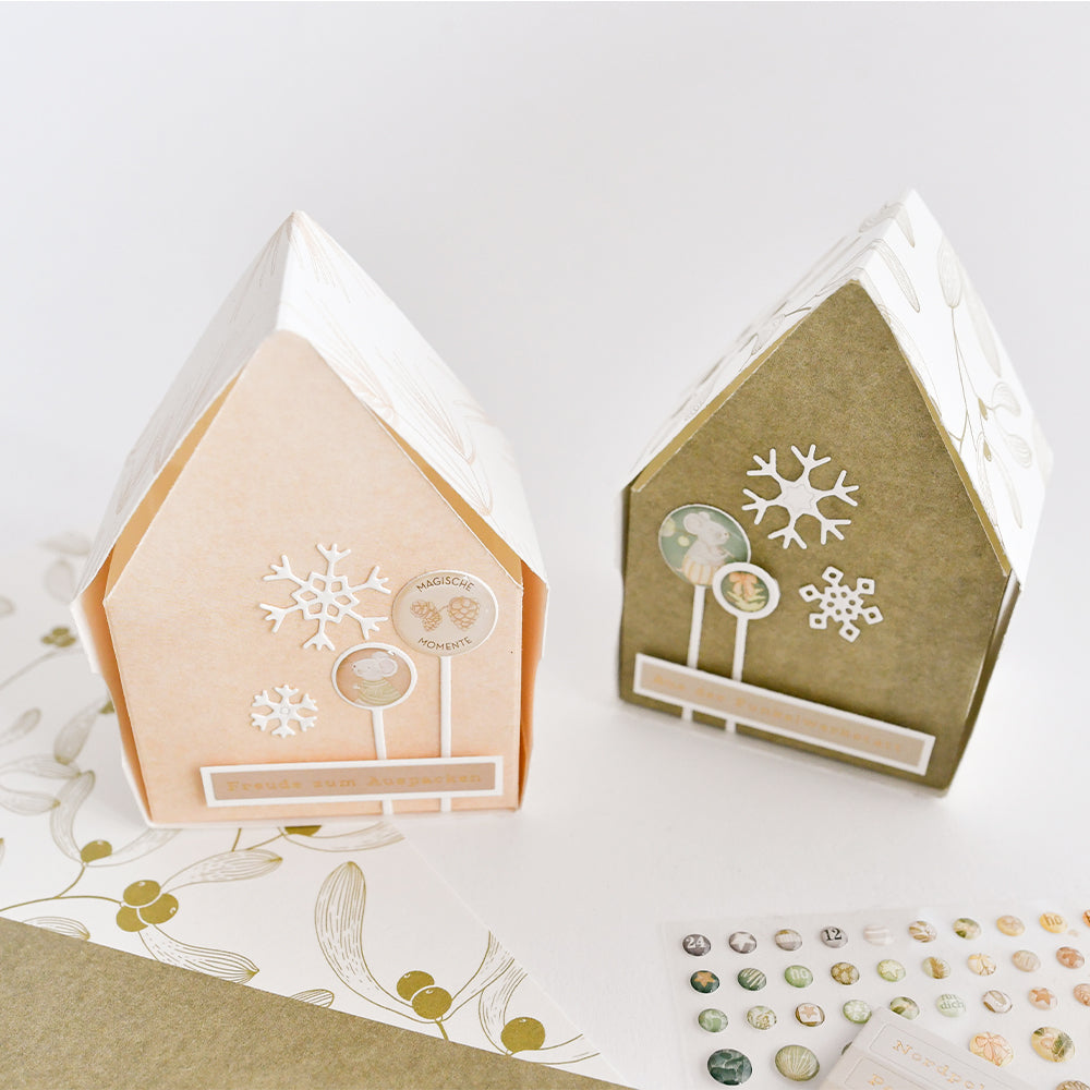 Zwei hausförmige Mimi Moosgrün-Geschenkboxen, verziert mit Schneeflocken- und Kreissymbolen.