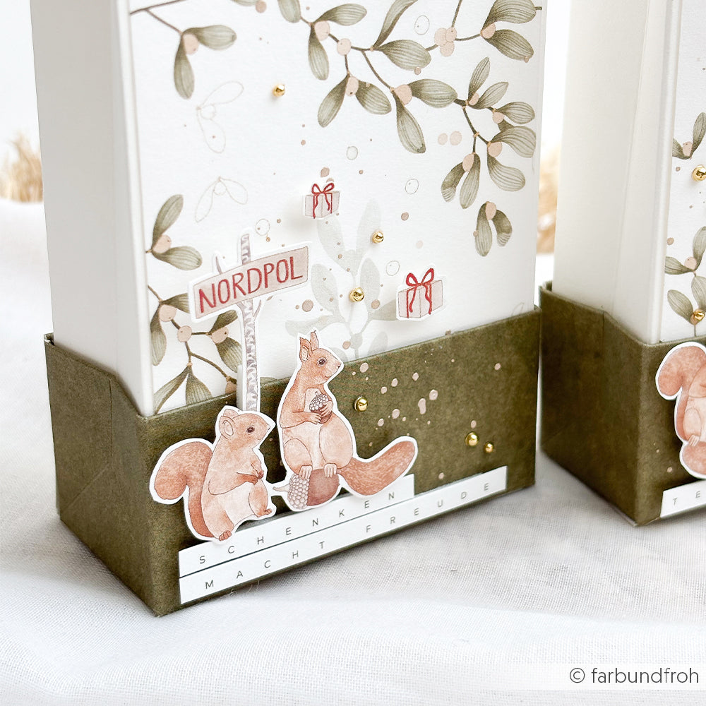 Zwei Mimi-Schattengrün-Geschenkboxen mit Eichhörnchen-Motiven, einem Nordpol-Schild und deutschem Text.