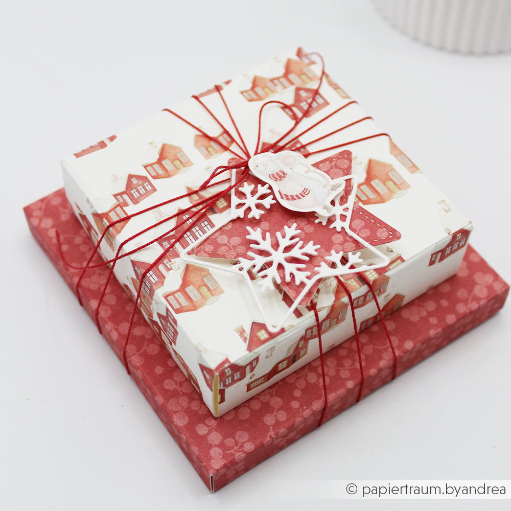 Zwei übereinander gestapelte Geschenkboxen aus hochwertigem Designpapier mit roter Schnur und Schneeflockenverzierungen.