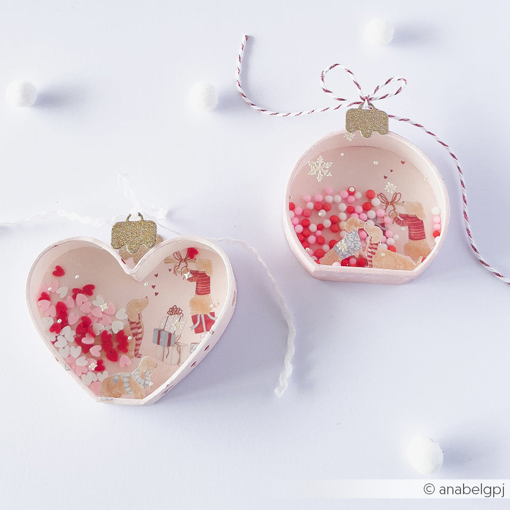 Zwei handgefertigte Papierprojekte-Weihnachtsanhänger mit Miniaturhunden, Geschenken und buntem Konfetti.