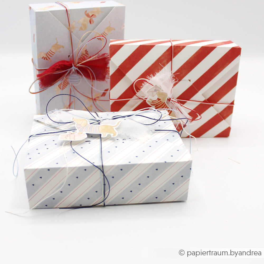 Drei Geschenkboxen, verpackt in Designpapier mit Hundemotiven und verziert mit Schleifen.