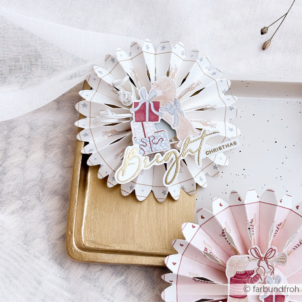 Runde Papierdekoration im Akkordeonstil mit Dackeln und Geschenkmotiven sowie der Aufschrift Bright Christmas.