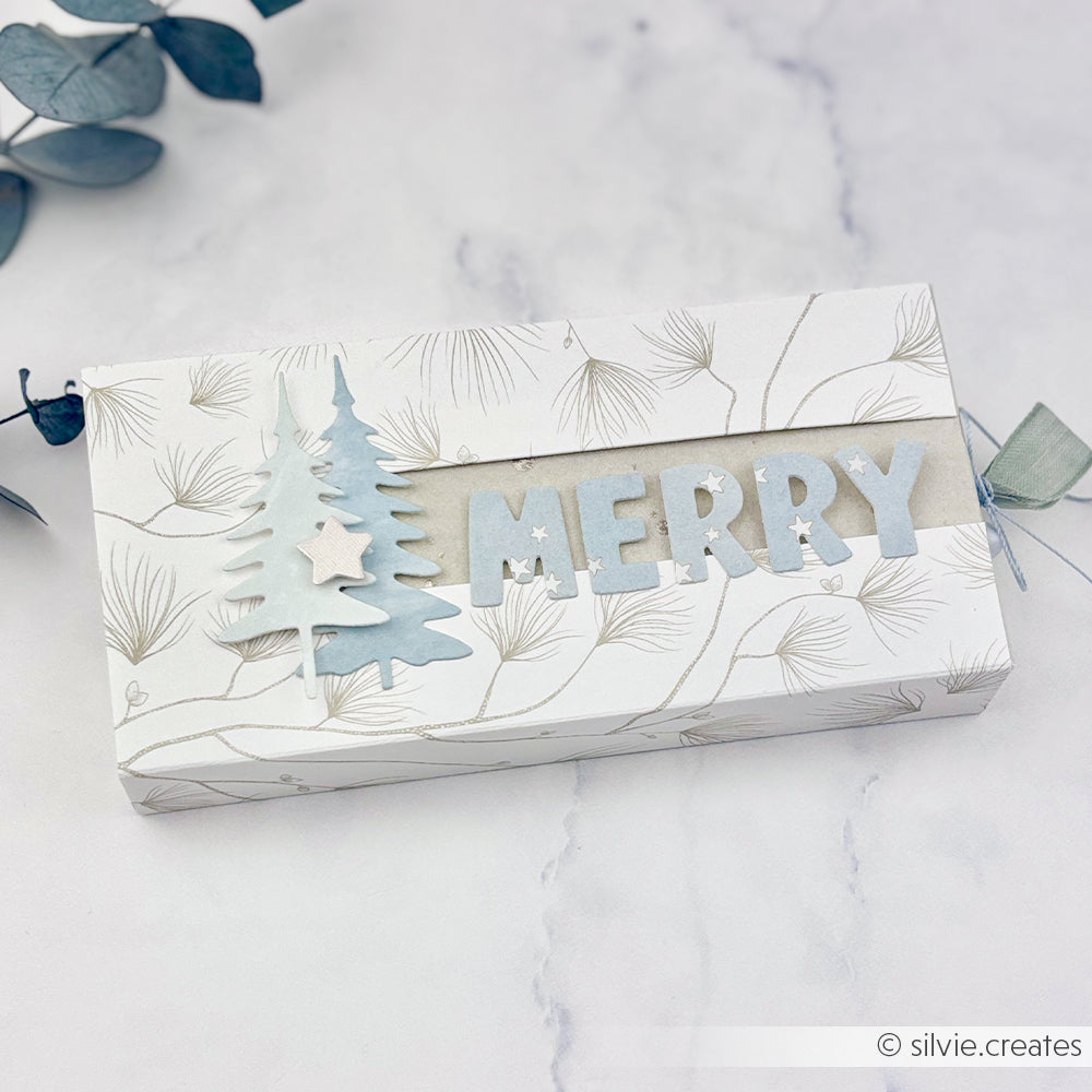 Eine rechteckige Geschenkbox mit einem Tannenbaum-Motiv und der Aufschrift MERRY auf dem Deckel für Papierbastelprojekte.