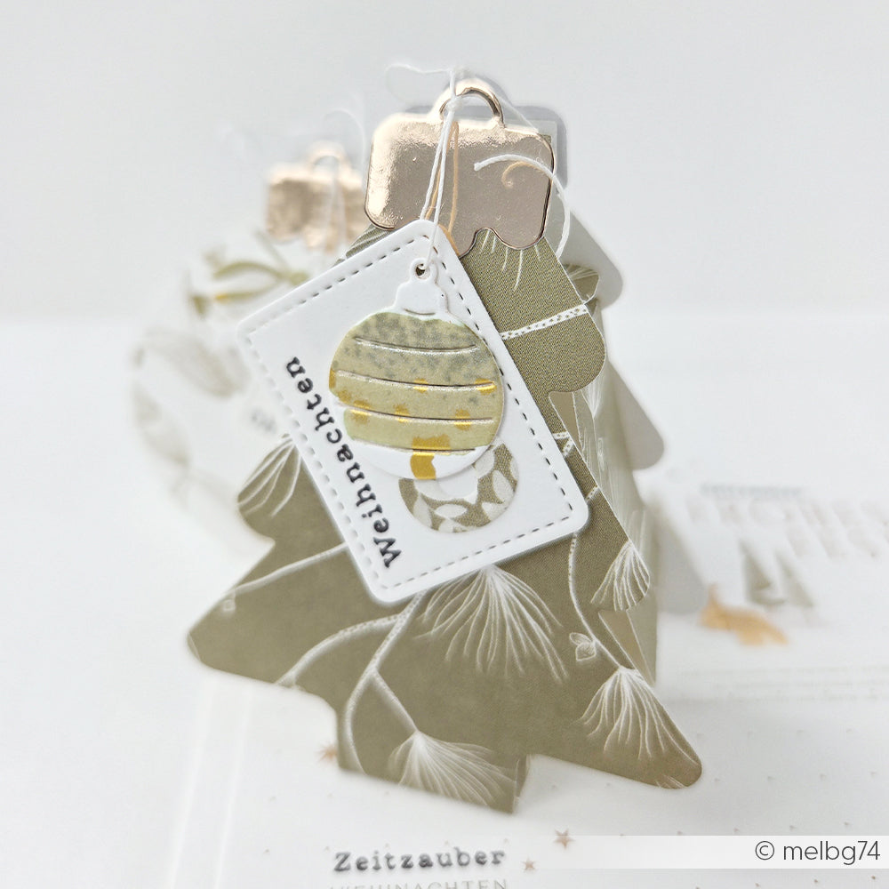 Olivgrüne Weihnachtsbaumkugel aus Papier mit Buchbinde-Motiv und einem Weihnachten-Anhänger.