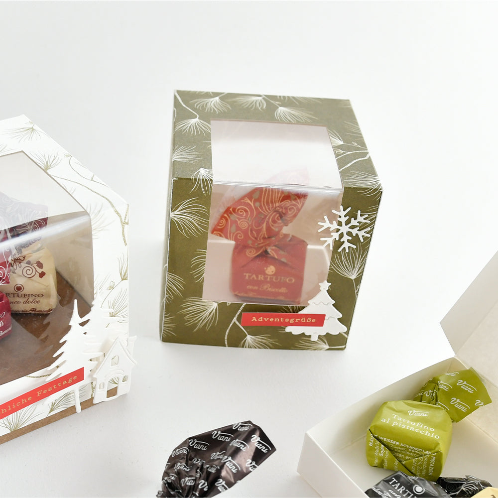 Drei Viani-Schokoladen-Geschenkboxen für die Feiertage sowie lose Pralinen in Verpackungen aus Designpapier.