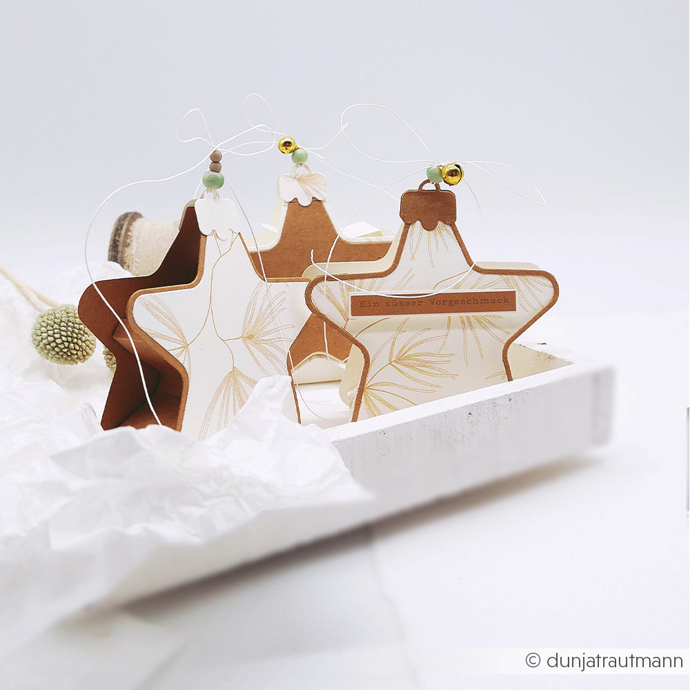 Drei sternförmige Geschenkboxen aus Designpapier auf einem weißen Tablett.