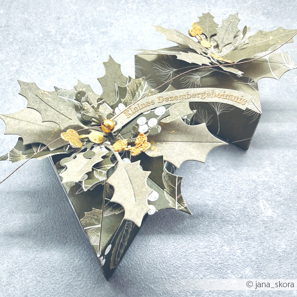 Zwei dunkelgrüne Geschenkboxen aus Designpapier, verziert mit Papierblättern in Stechpalmenform und goldenen Akzenten.