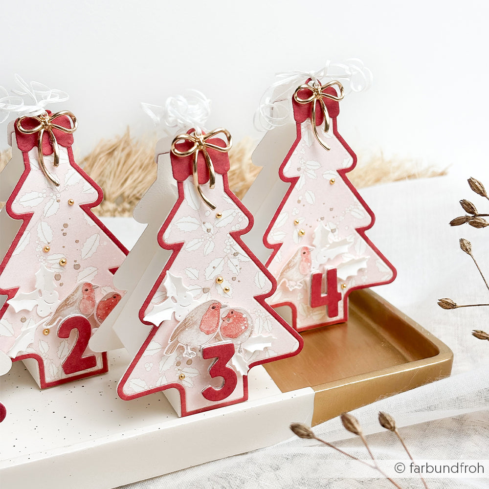 Drei weihnachtsbaumförmige Adventskalender-Schachteln aus Designpapier auf einem goldenen Tablett.