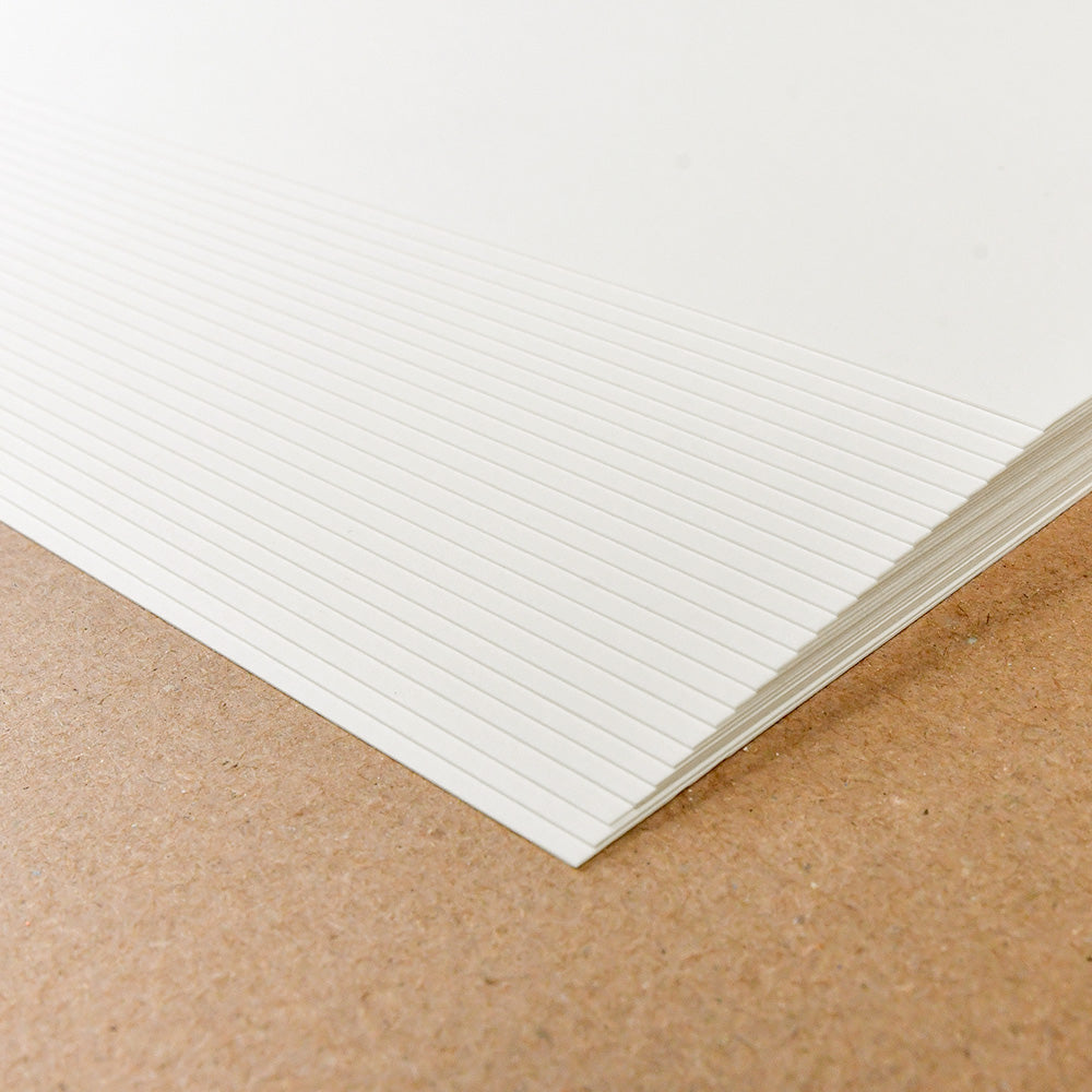 Ein Stapel von Alexandra Renke cremeweißes Designpapier mit horizontalen Linien ruht auf einer braunen Oberfläche, perfekt für Buchbindearbeiten oder jedes kreative Projekt.