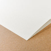 Ein Stapel von Alexandra Renke cremeweißes Designpapier mit horizontalen Linien ruht auf einer braunen Oberfläche, perfekt für Buchbindearbeiten oder jedes kreative Projekt.